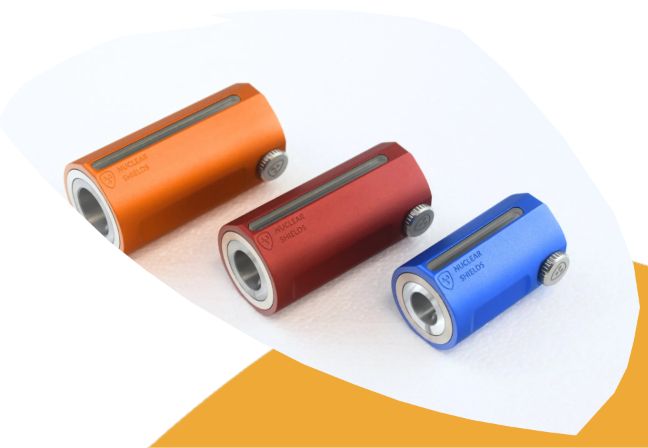 Three cylindrical magnetic components labeled 'MAGNET SHIELD' in orange, red, and blue, arranged diagonally on a white background with a yellow accent shape.